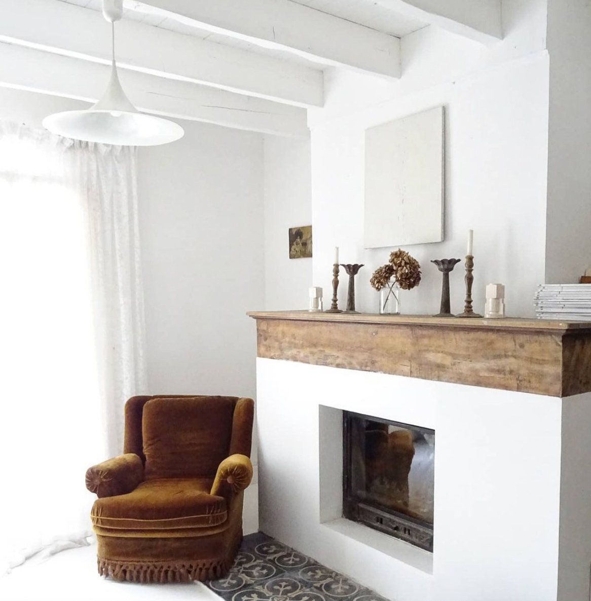 White interior with vintage velvet chair and large fireplace with vintage accessories