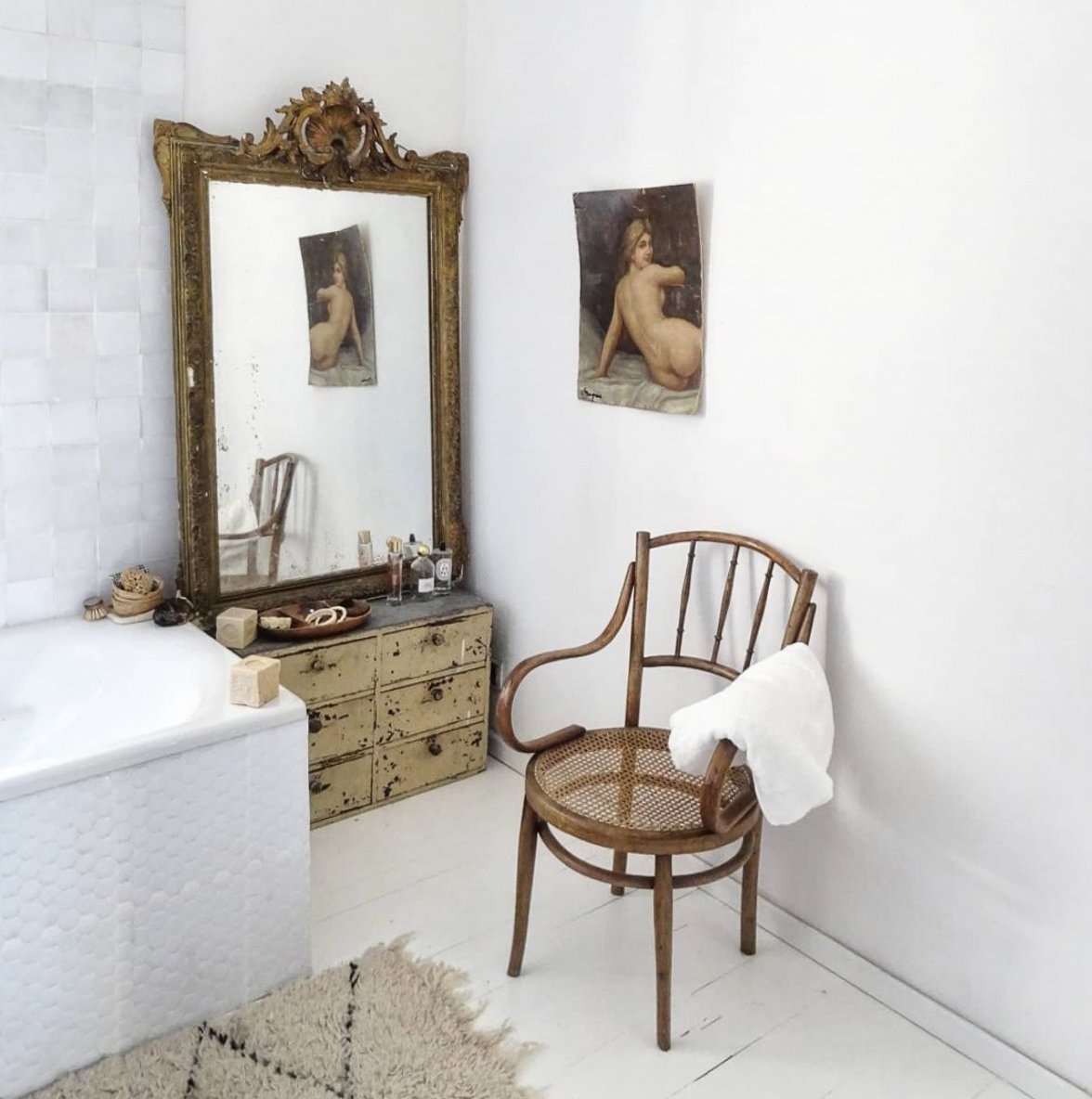 White interior of bathroom with vintage chair and large gilded mirror