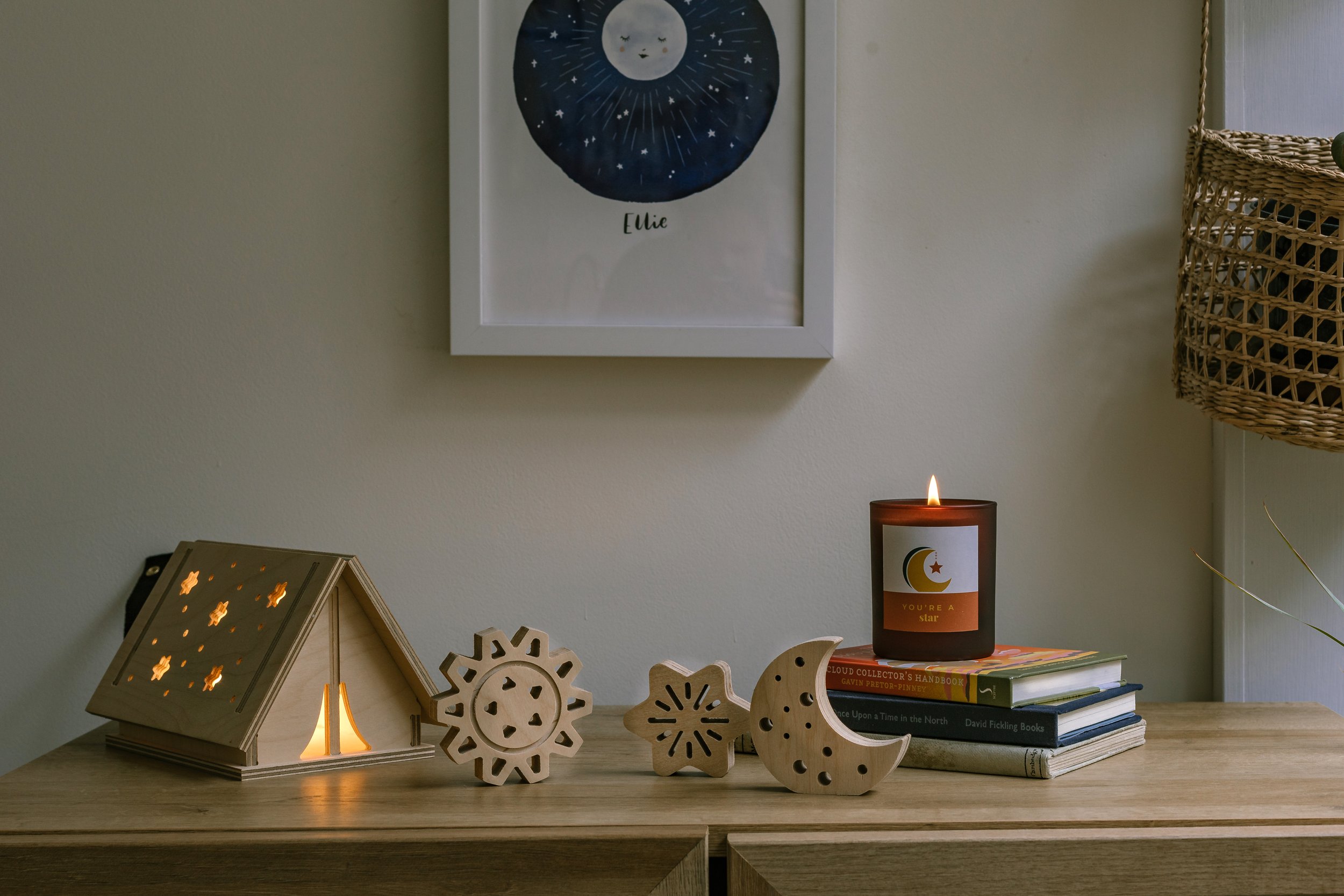 tabletop with plywood tent-shaped light, wooden decorations, books and candle