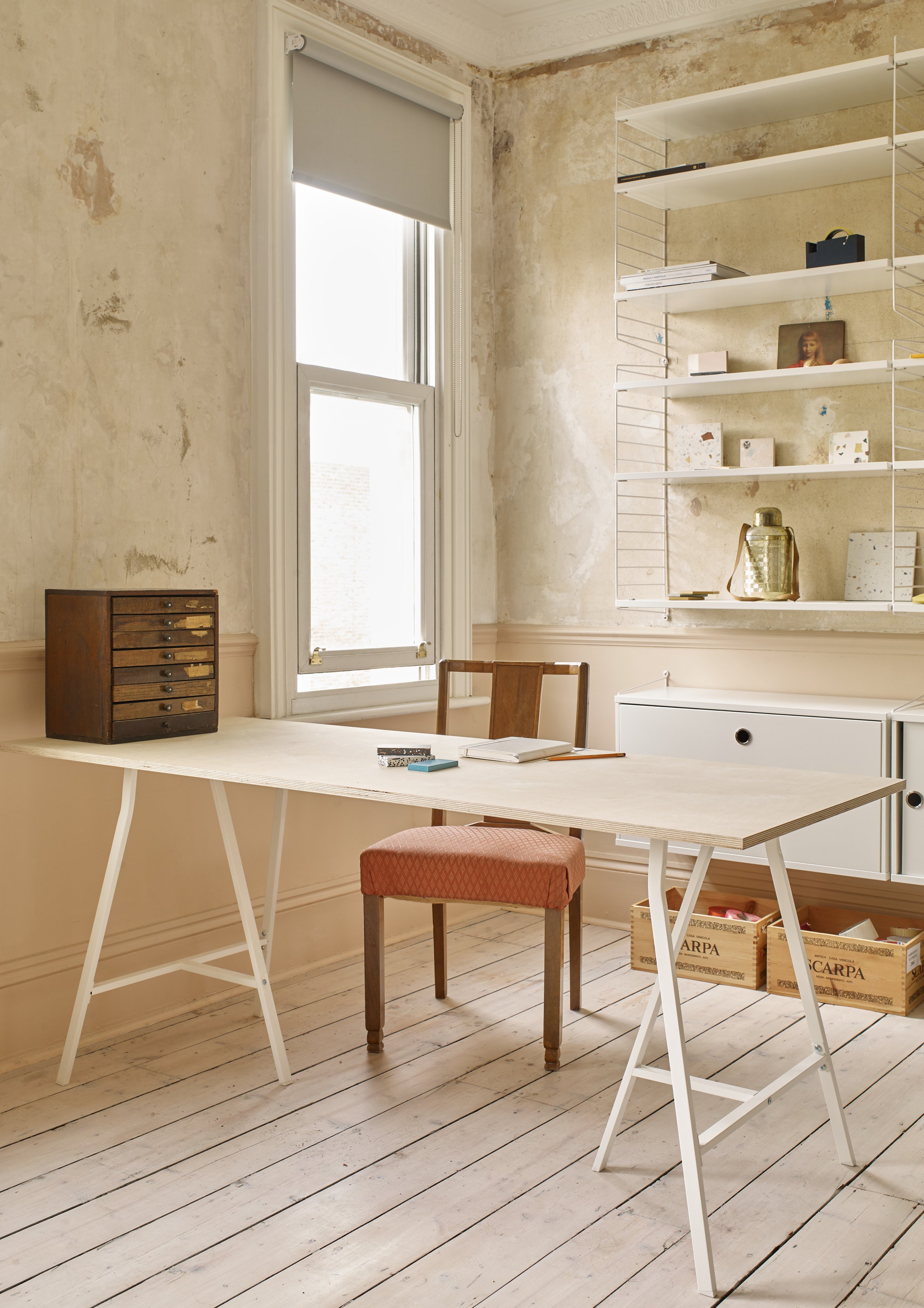 home office space with bare plaster walls, plywood desk and modern shelving