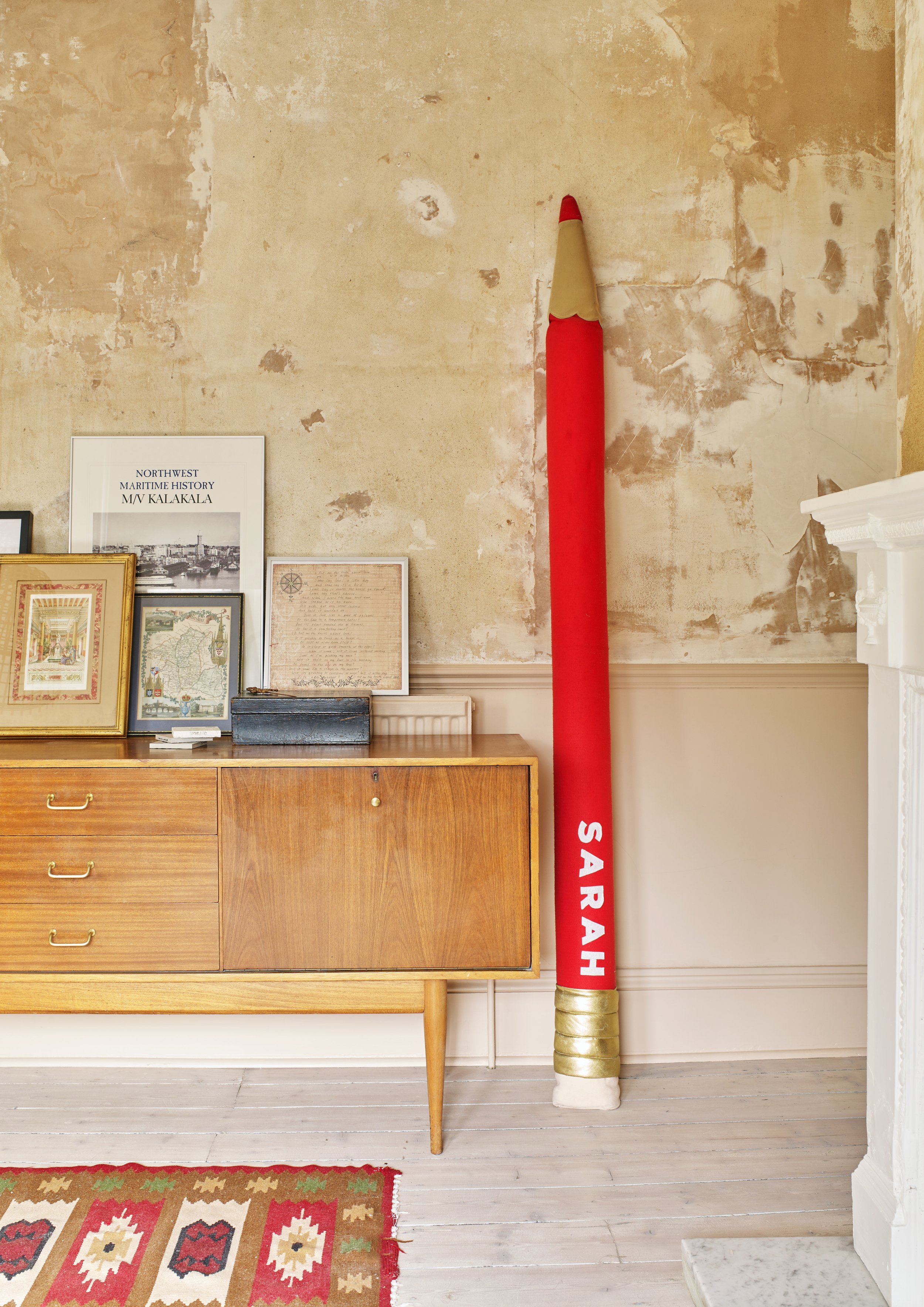 Bare plaster walls with giant red pencil and a mid century sideboard