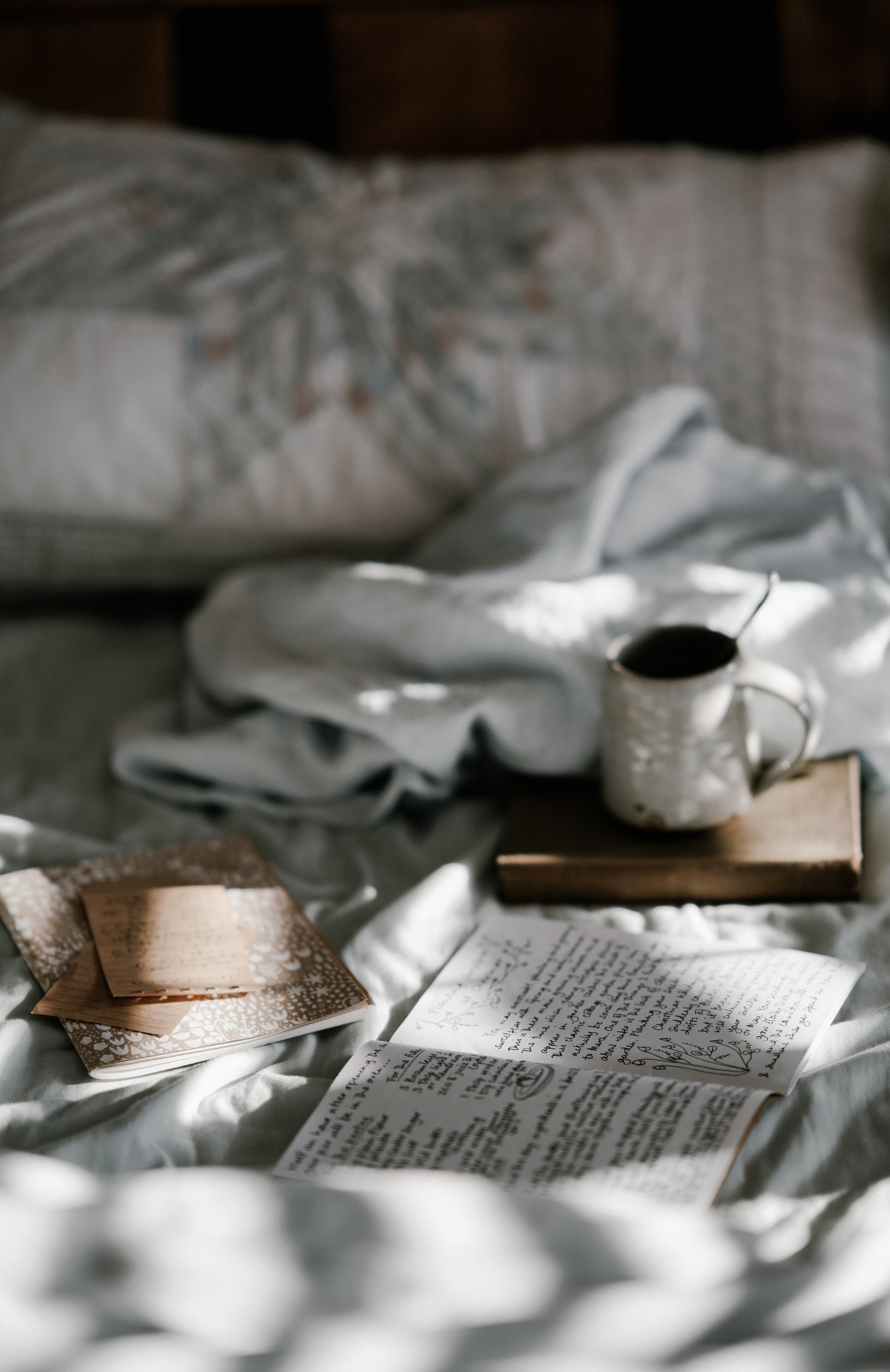 a messy bed with notebooks and a coffee cup, with sunlight filtering through