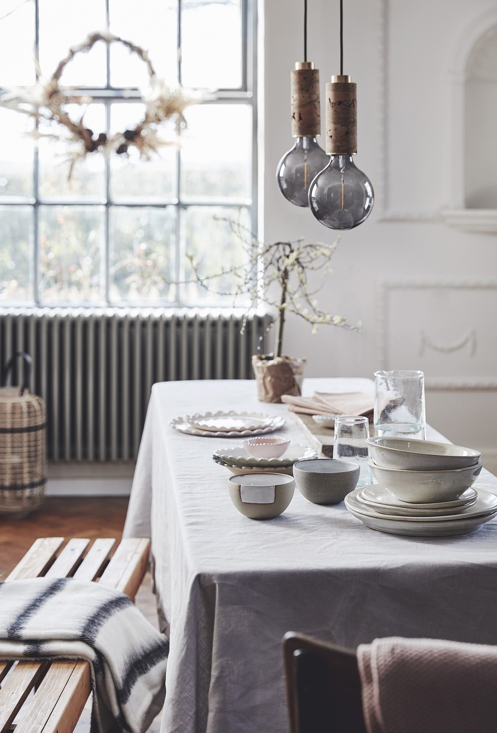 ceramic plates and bowls and small bowls in foreground by Camphill Village Trust - Small Batch Goods; Fluted edge hand made tableware – Kchossack Pottery; Avocado dyed hemp napkins – Small Batch Goods; Glassware – Form Lifestyle; Blanket on bench – …