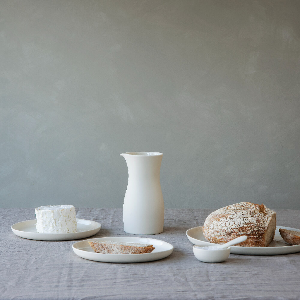 Minimal white tableware by British ceramist Sue Pyrke on grey linen tablecloth