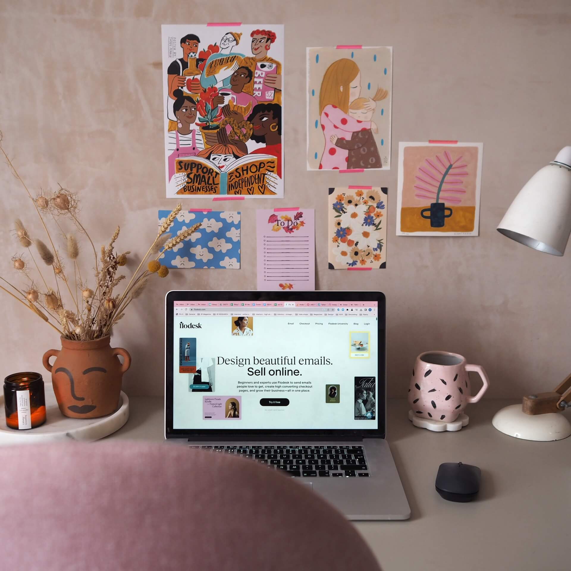 Email marketing tips from 91 Magazine - laptop displaying Flodesk home page, at a desk in a home office, with colourful picture on bare plaster wall. 