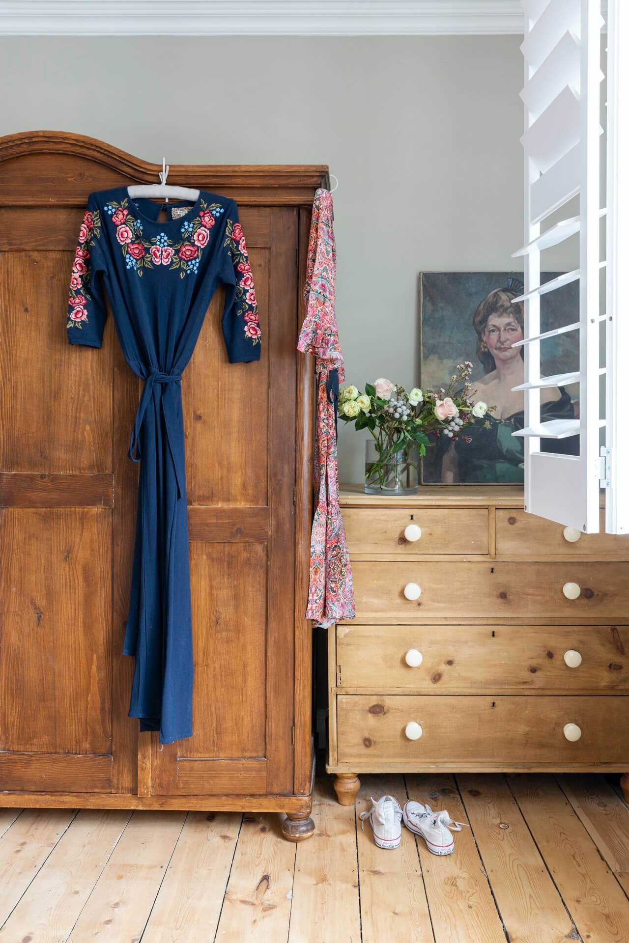 vintage wooden wardrobe and drawers with pretty dress hanging up, flowers and vintage portrait painting on display