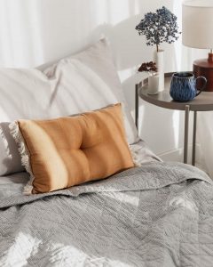 Ochre cushion on a bed and other items from lifestyle store Tusk