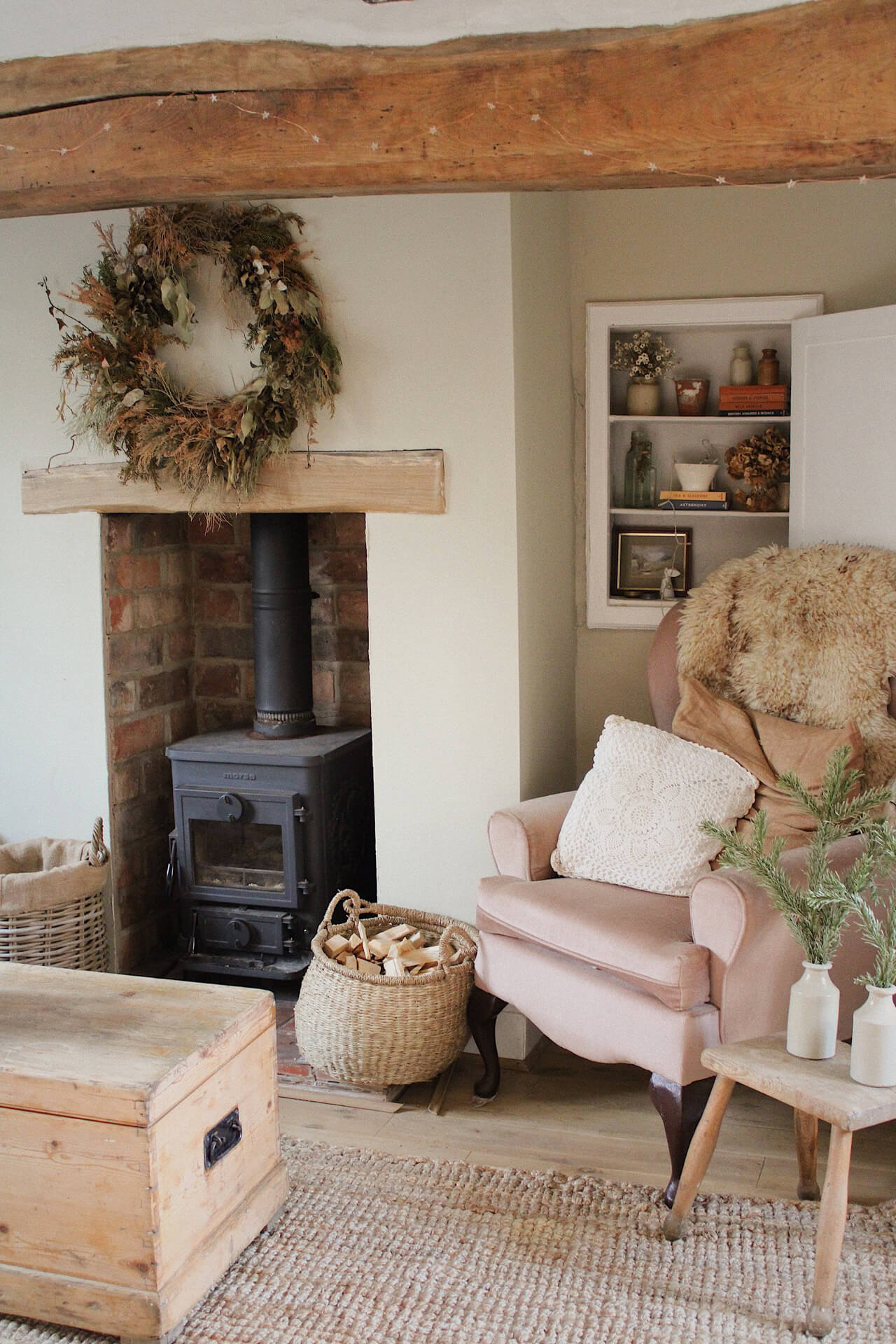 Home tour with Rachel Ashfield of @the_old_cottage - a cosy corner in the old cottage living room with a wood burner, a large dried wreath and a pink armchair