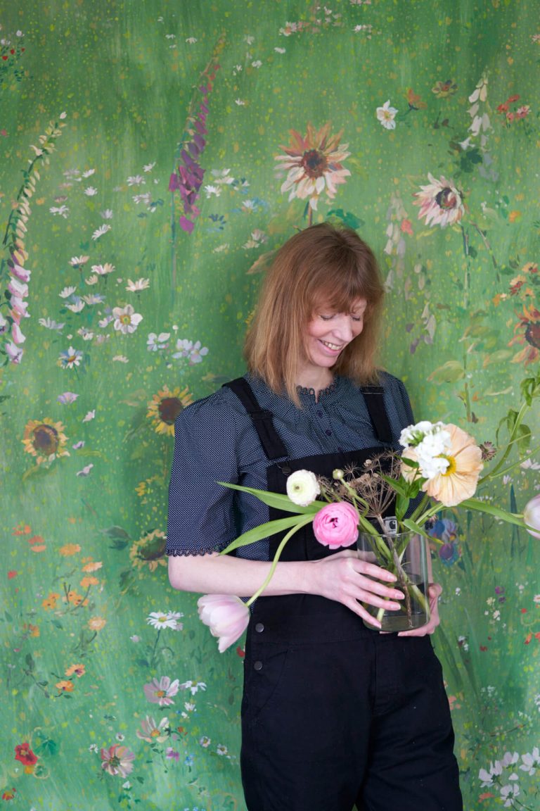 Wallpaper designer Flora Roberts in front of floral green wallpaper
